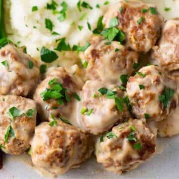 Swedish meatballs with creamy sauce, mashed potatoes, green beans, and lingonberry sauce on a plate.