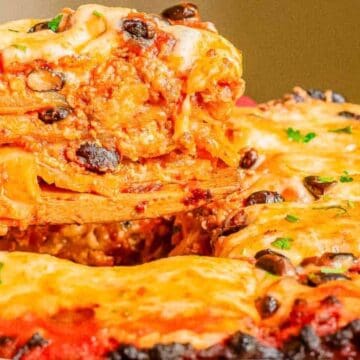 A close-up of cheesy baked lasagna with black olives, being served from a casserole dish with a wooden spatula.