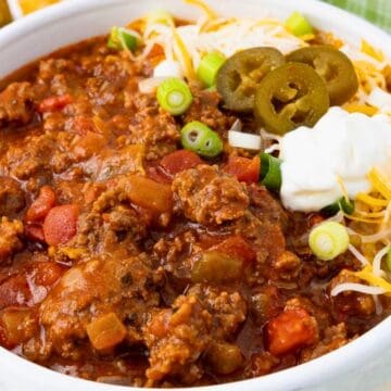 Bowl of chili topped with shredded cheese, sour cream, sliced green onions, and jalapeños.