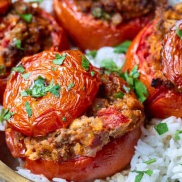 Stuffed tomatoes with herbs, served over white rice on a plate with a spoon on the side.