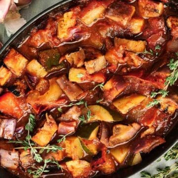 Oven-baked ratatouille with colorful vegetables and herbs in a black dish, garnished with fresh thyme.