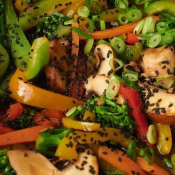 Colorful vegetable stir-fry with broccoli, mushrooms, peppers, scallions, and black sesame seeds.
