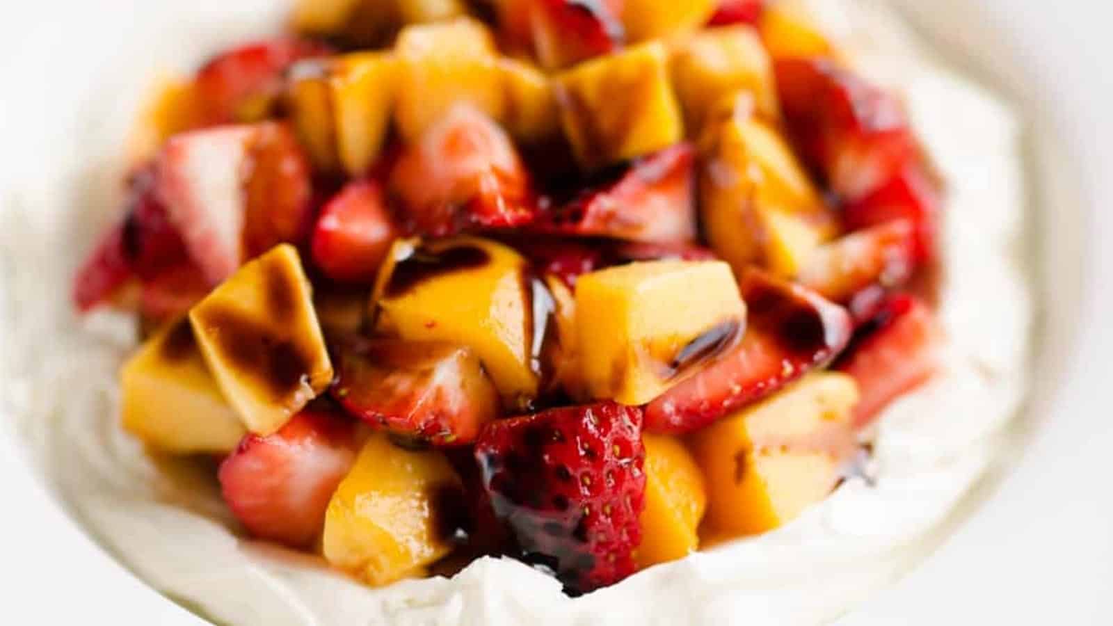 A close-up of chopped strawberries and mango on whipped cream, drizzled with balsamic glaze.