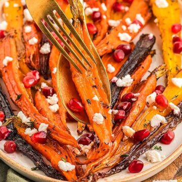 Plate of roasted heirloom carrots topped with goat cheese and pomegranate seeds; a fork and knife cutting a carrot—a vibrant addition to your favorite carrot recipes.