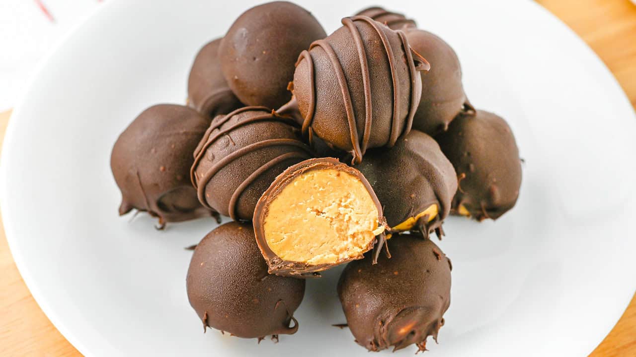 A plate of chocolate-covered peanut butter balls, with one cut in half showing the creamy peanut butter filling inside.
