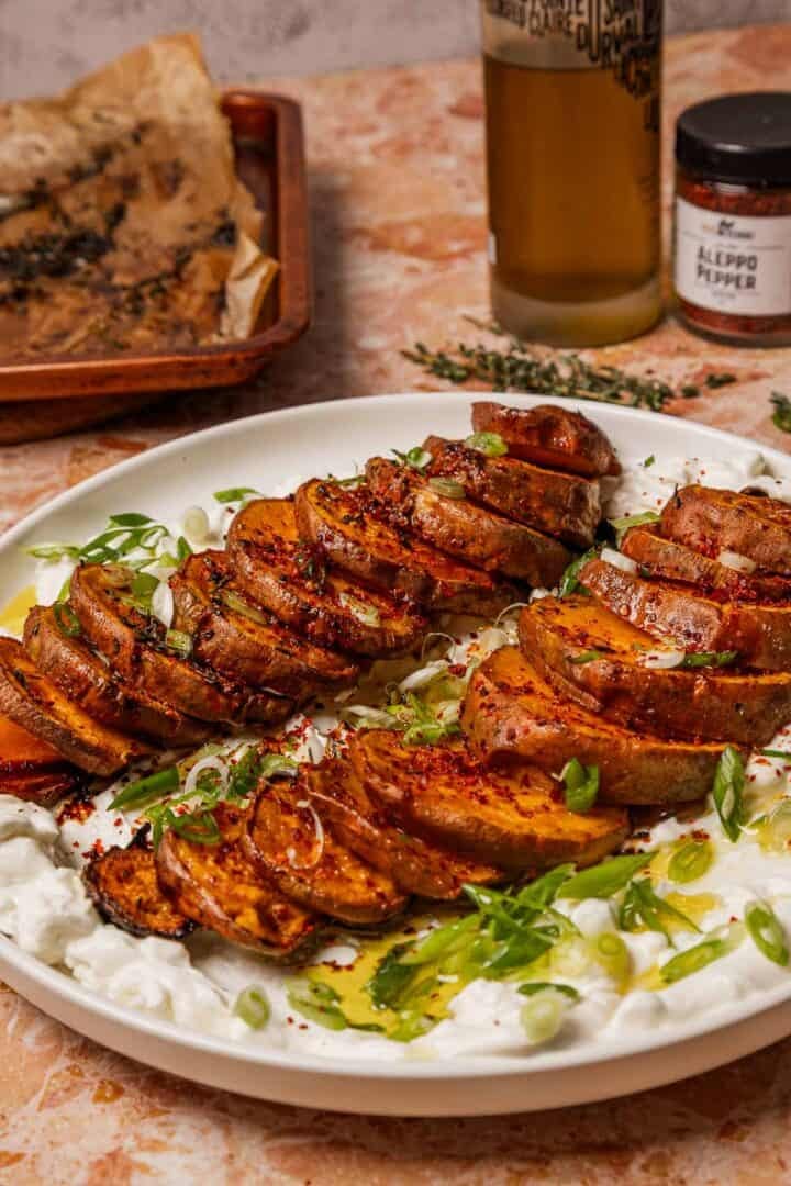 Caramelized sweet potato slices rest on whipped feta, garnished with green onions and spices on a white plate.