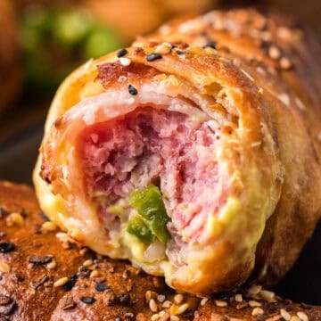 A close-up of a pastry filled with ham, cheese, and green pepper, topped with sesame and poppy seeds.