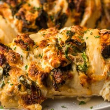 Stuffed chicken breast with melted cheese, herbs, and vegetables on a white plate.
