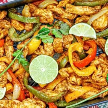 Colorful chicken fajitas with sliced bell peppers, onions, cilantro, and lime wedges in a baking tray.