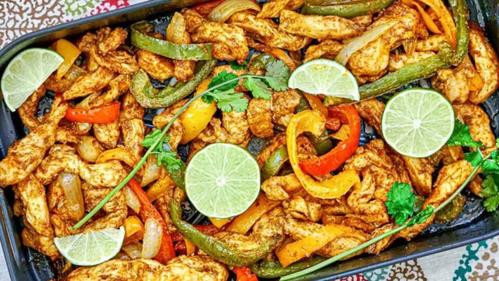 A tray of chicken fajitas with bell peppers, onions, lime slices, and cilantro garnish.