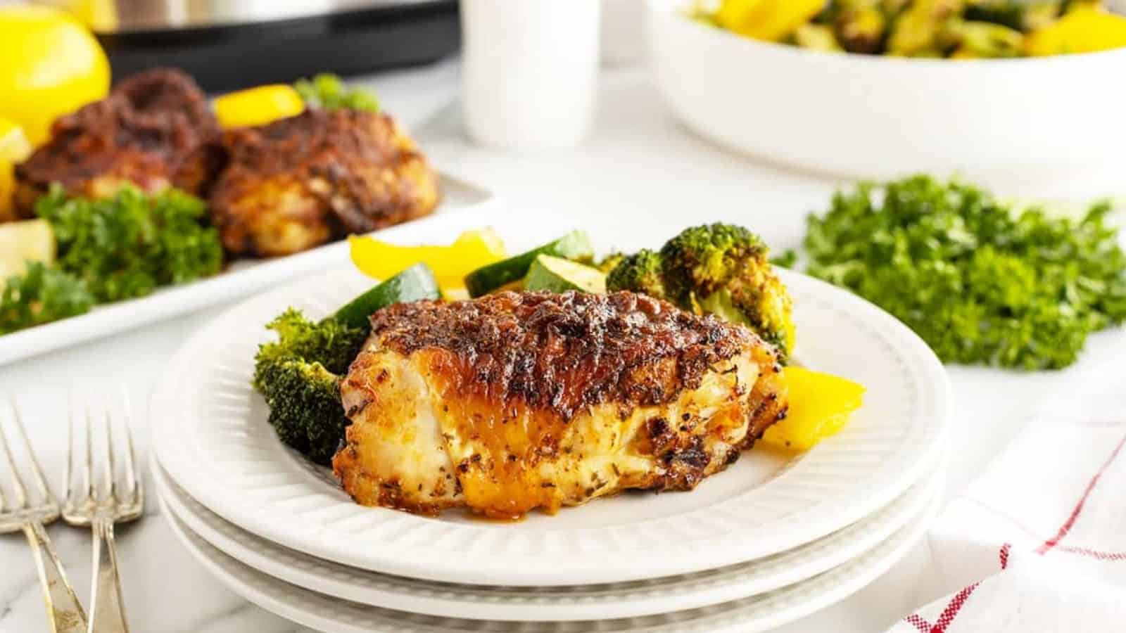 Grilled seasoned chicken breast with roasted vegetables on a white plate, garnished with fresh parsley.