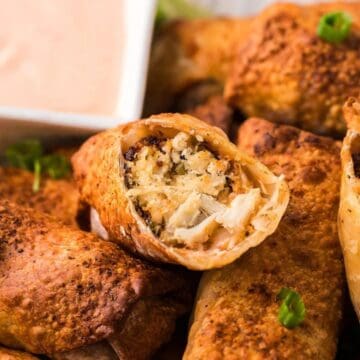 Close-up of crispy egg rolls, one split open to reveal filling, with a creamy dipping sauce in the background.