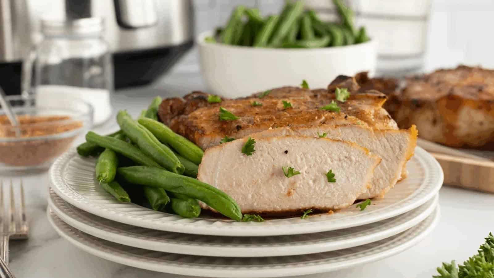 Sliced pork chop with green beans on a white plate, garnished with parsley.