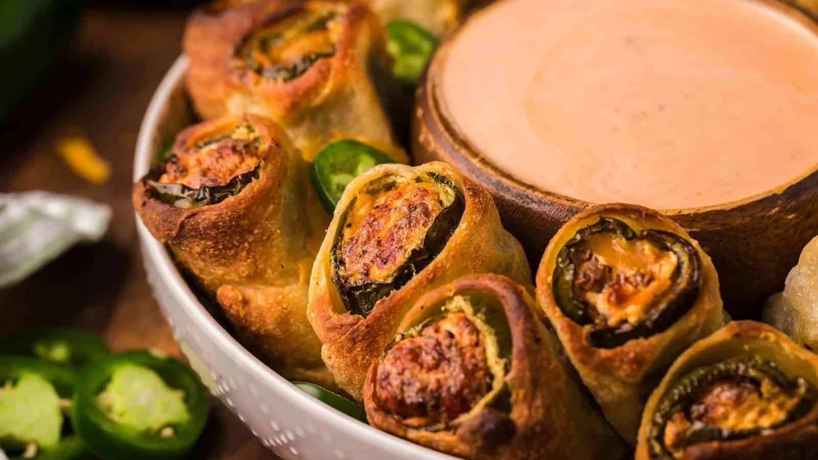 Close-up of jalape&ntilde;o popper rolls in a bowl, served with a side of creamy dipping sauce.