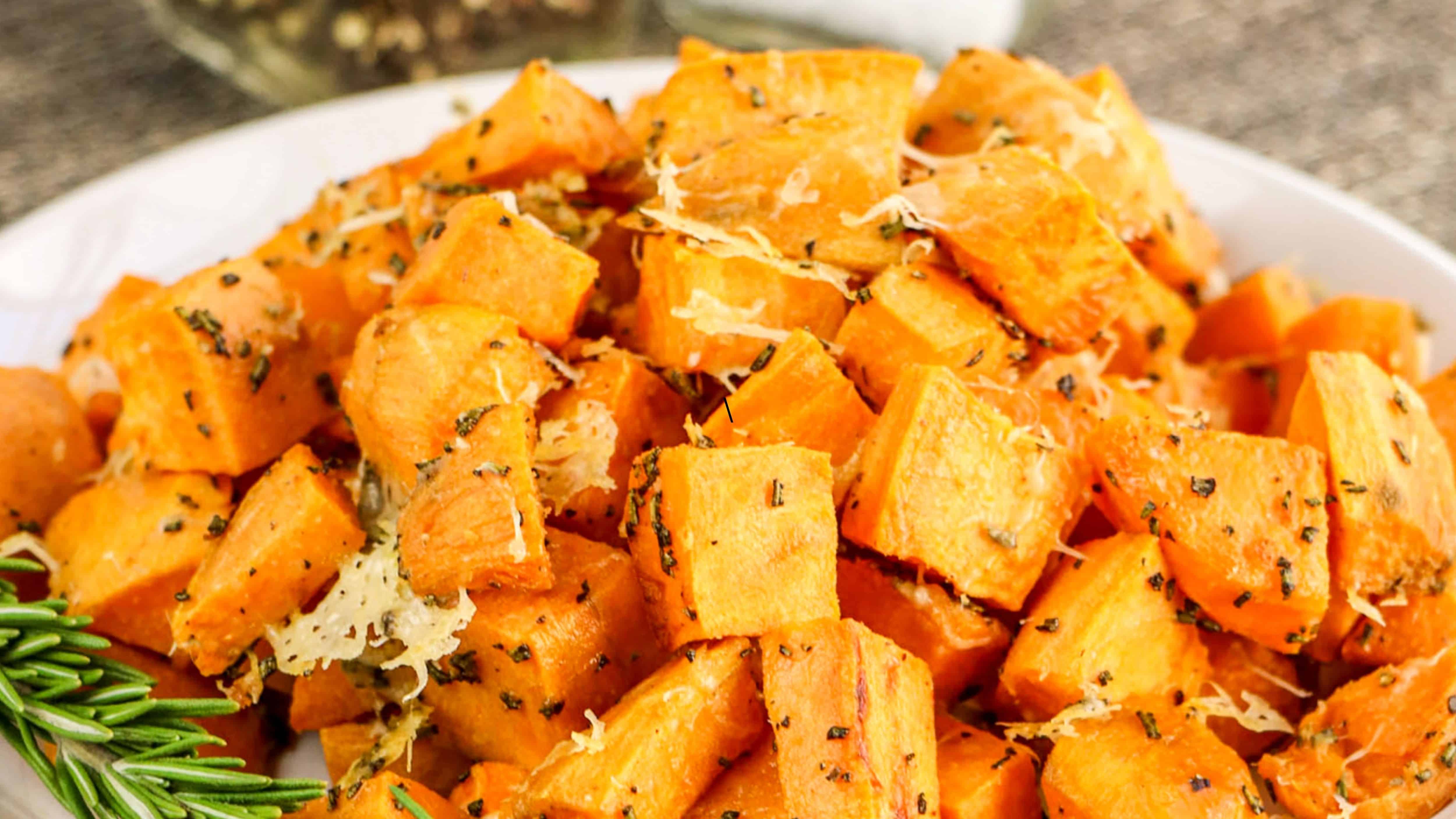 A plate of roasted sweet potato cubes, garnished with herbs and shredded cheese.