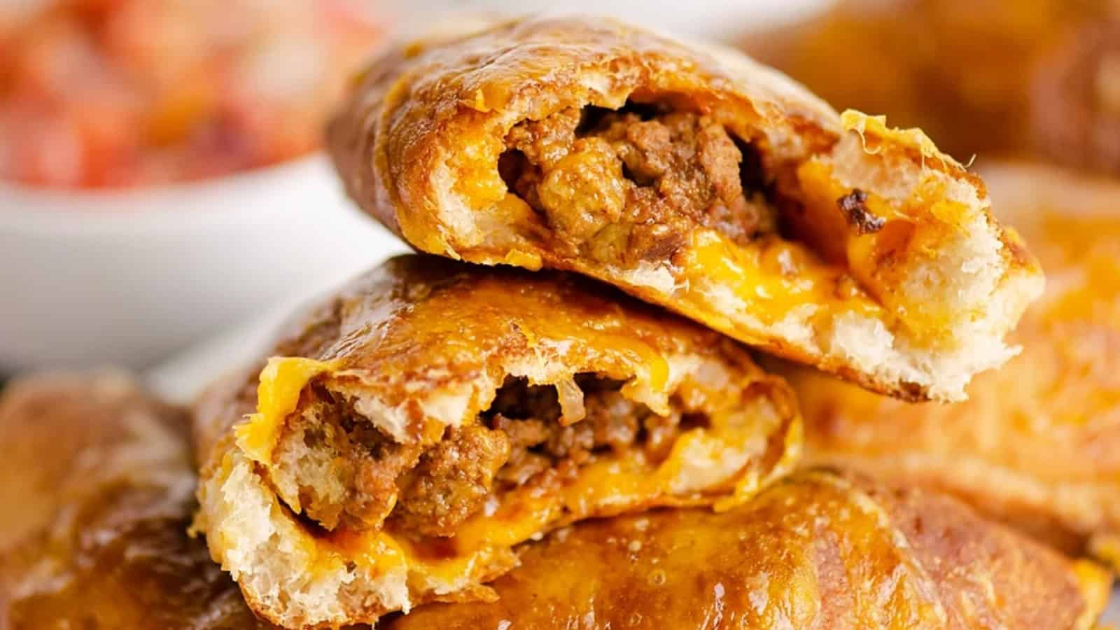 Two golden-brown meat and cheese-filled pastries stacked, with the flaky insides and filling visible.