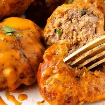 Close-up of cheesy meatballs topped with herbs, one cut open with a fork showing the inside texture.