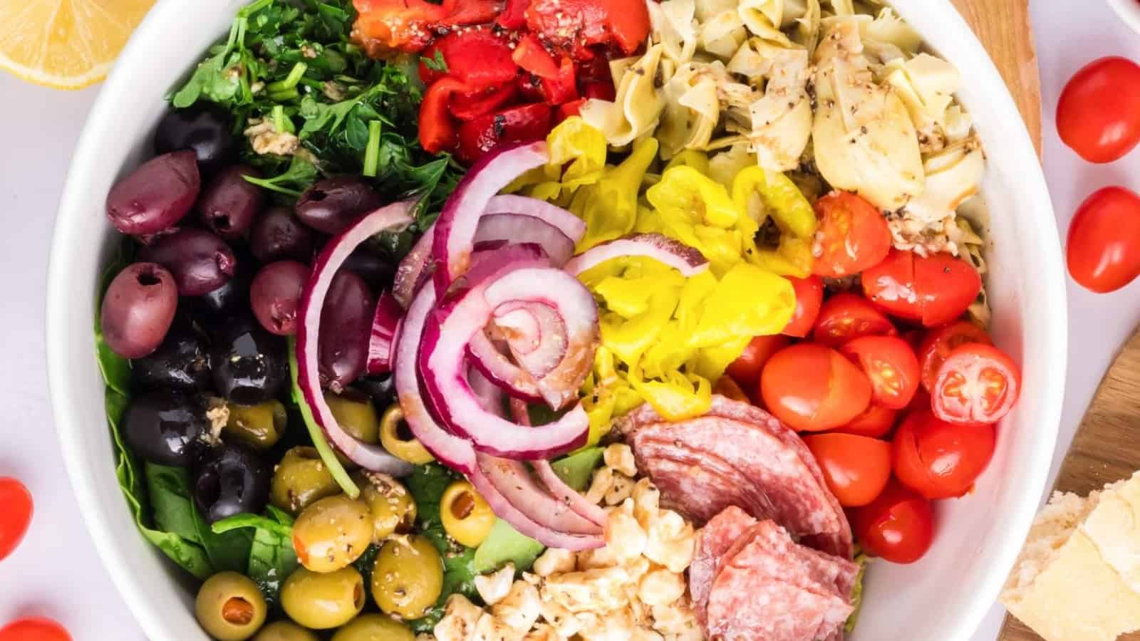 A bowl filled with olives, onions, tomatoes, salami, artichokes, peppers, parsley, and cheese.