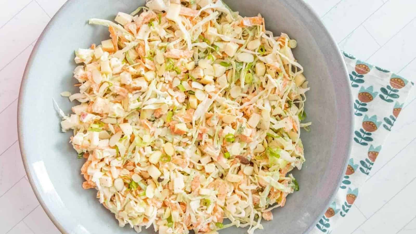 A bowl of coleslaw with shredded cabbage, carrots, and chopped vegetables on a white table.