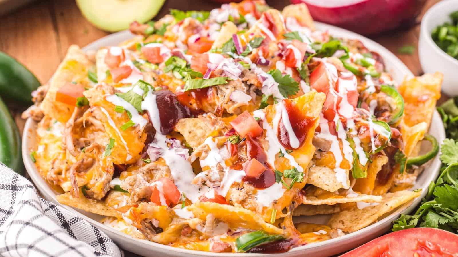 A plate of loaded nachos topped with cheese, sour cream, barbecue sauce, tomatoes, and fresh cilantro.