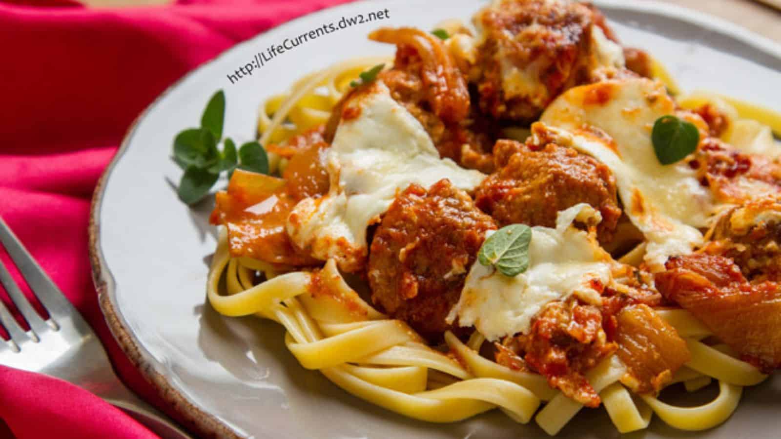 Plate of fettuccine topped with meatballs, tomato sauce, melted cheese, and fresh herbs on a table.