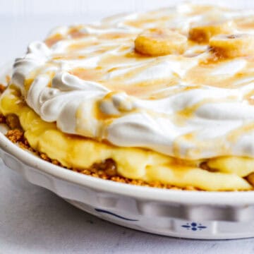 Banana cream pie topped with whipped cream and caramel drizzle in a white pie dish.