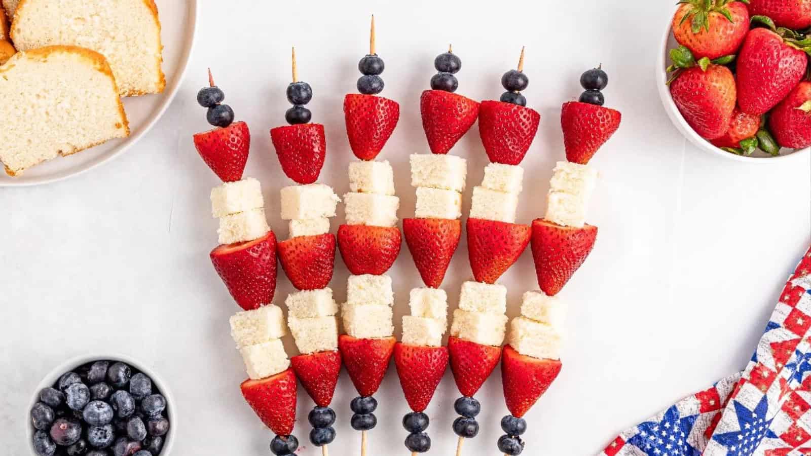 Fruit and pound cake skewers with strawberries, blueberries, and cake cubes, arranged on a white background.