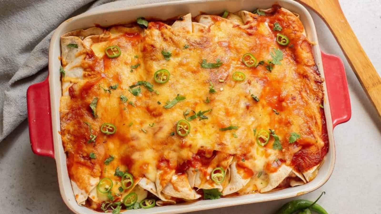 A baking dish of cheesy enchiladas topped with sliced green chilies and fresh cilantro.