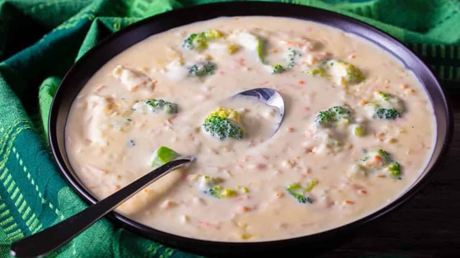 A bowl of creamy broccoli and cheese soup with a spoon, set on a green cloth.