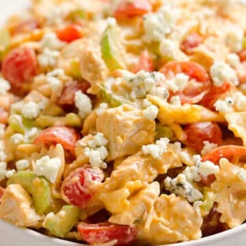Bowl of pasta salad with tomatoes, celery, chicken, and crumbled blue cheese on top.