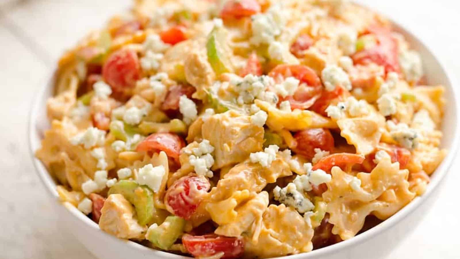 Bowl of pasta salad with tomatoes, celery, chicken, and crumbled blue cheese on top.