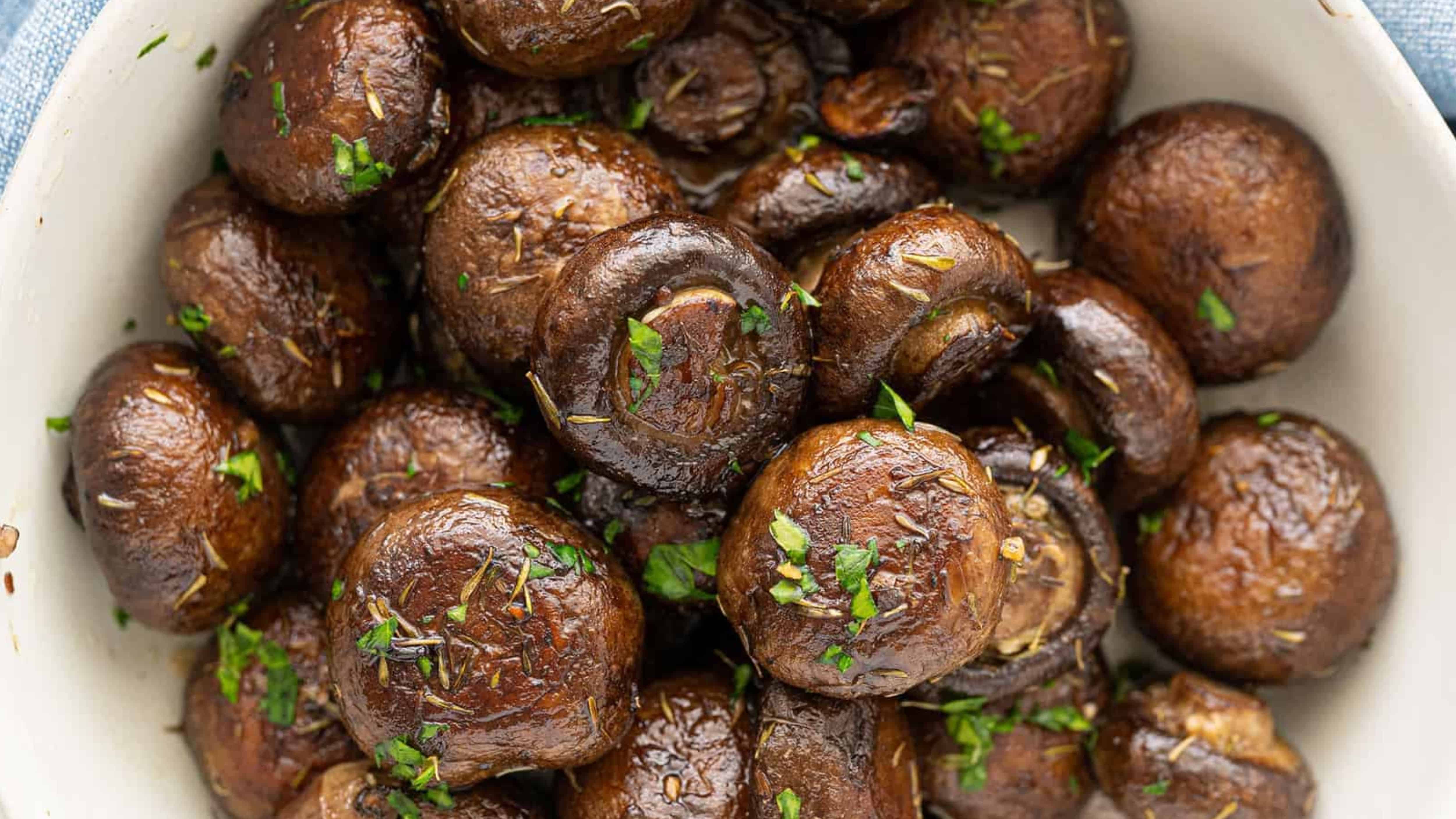 Brown roasted mushrooms garnished with chopped herbs in a white bowl.