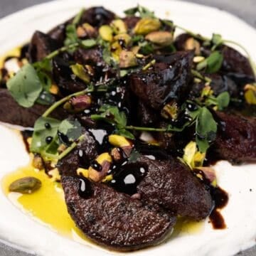 Cast-Iron Charred Beet Salad features roasted beets with balsamic glaze, pistachios, and fresh herbs on a bed of creamy white sauce.
