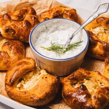 Golden baked pastries with a creamy dill dip in the center, served on a tray lined with parchment paper.