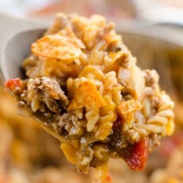 A spoonful of cheesy taco pasta with ground beef, tomatoes, and crushed tortilla chips.