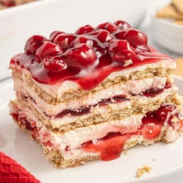 A slice of cherry dessert with careamy layers and graham crackers on a white plate.