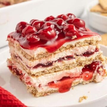A slice of layered cherry dessert with graham crackers and cream is served on a white plate.