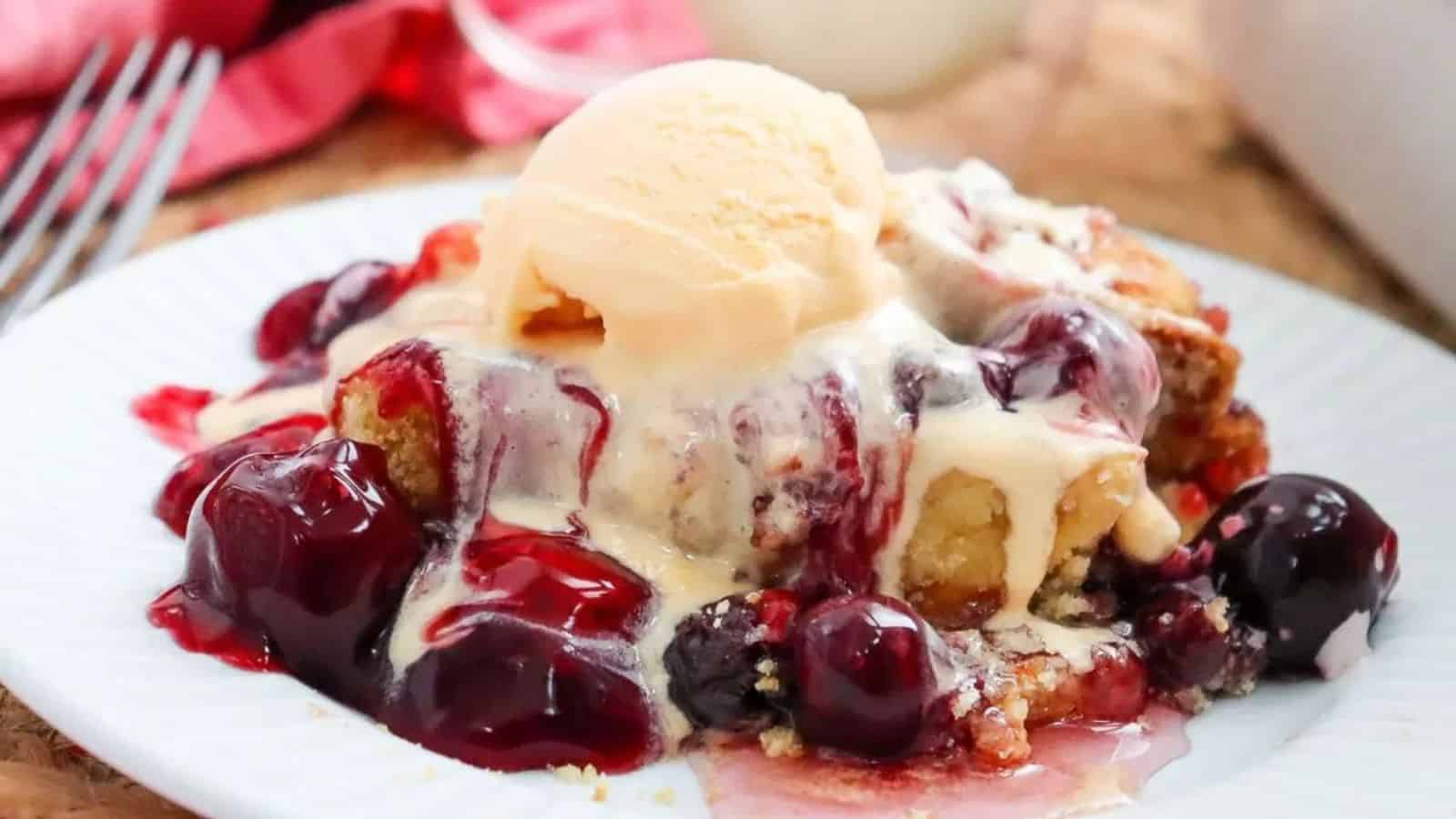 A serving of cherry cobbler with vanilla ice cream melting on top, on a white plate.