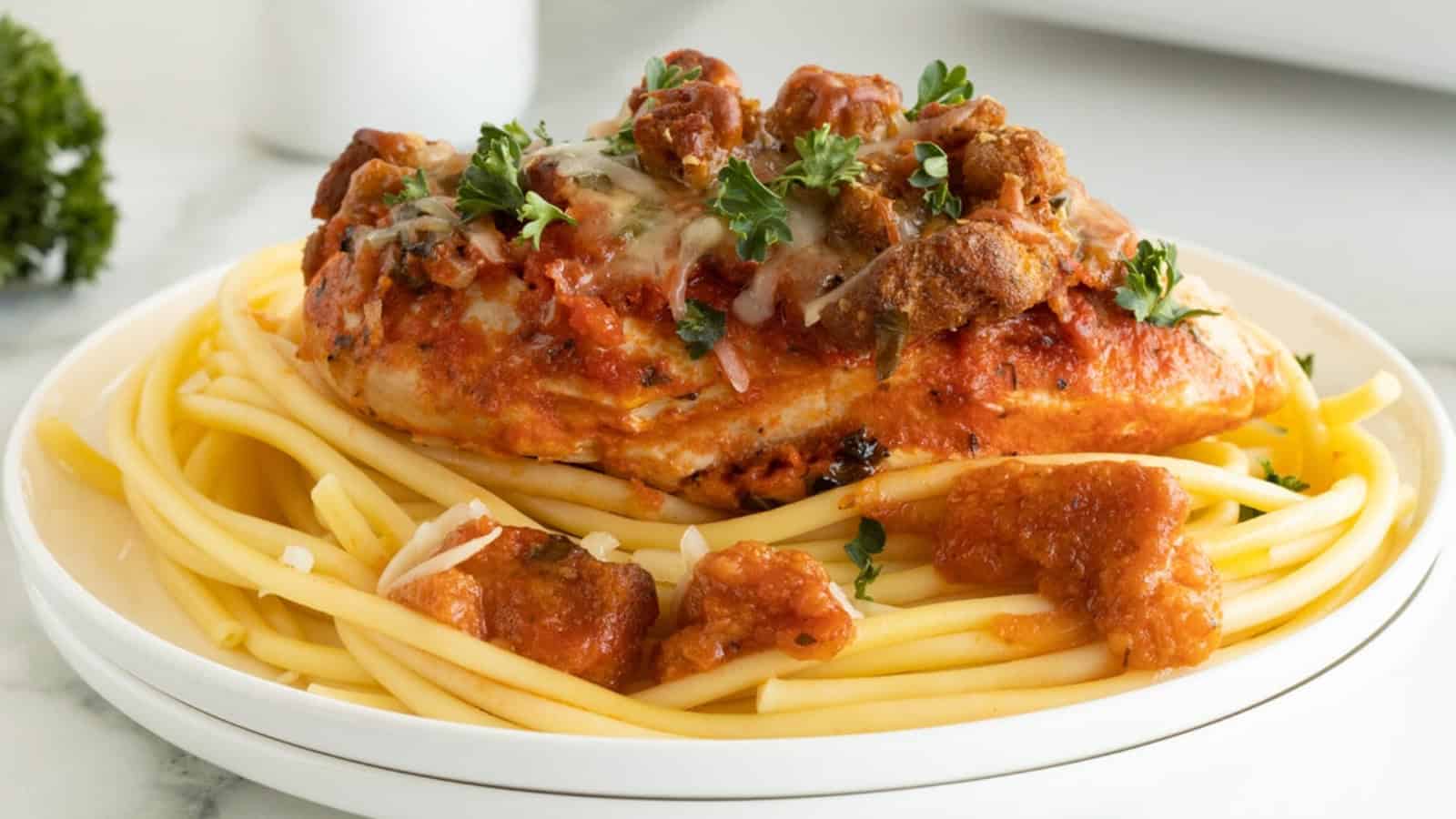 Chicken parmesan with marinara sauce served over a bed of spaghetti noodles, garnished with parsley.
