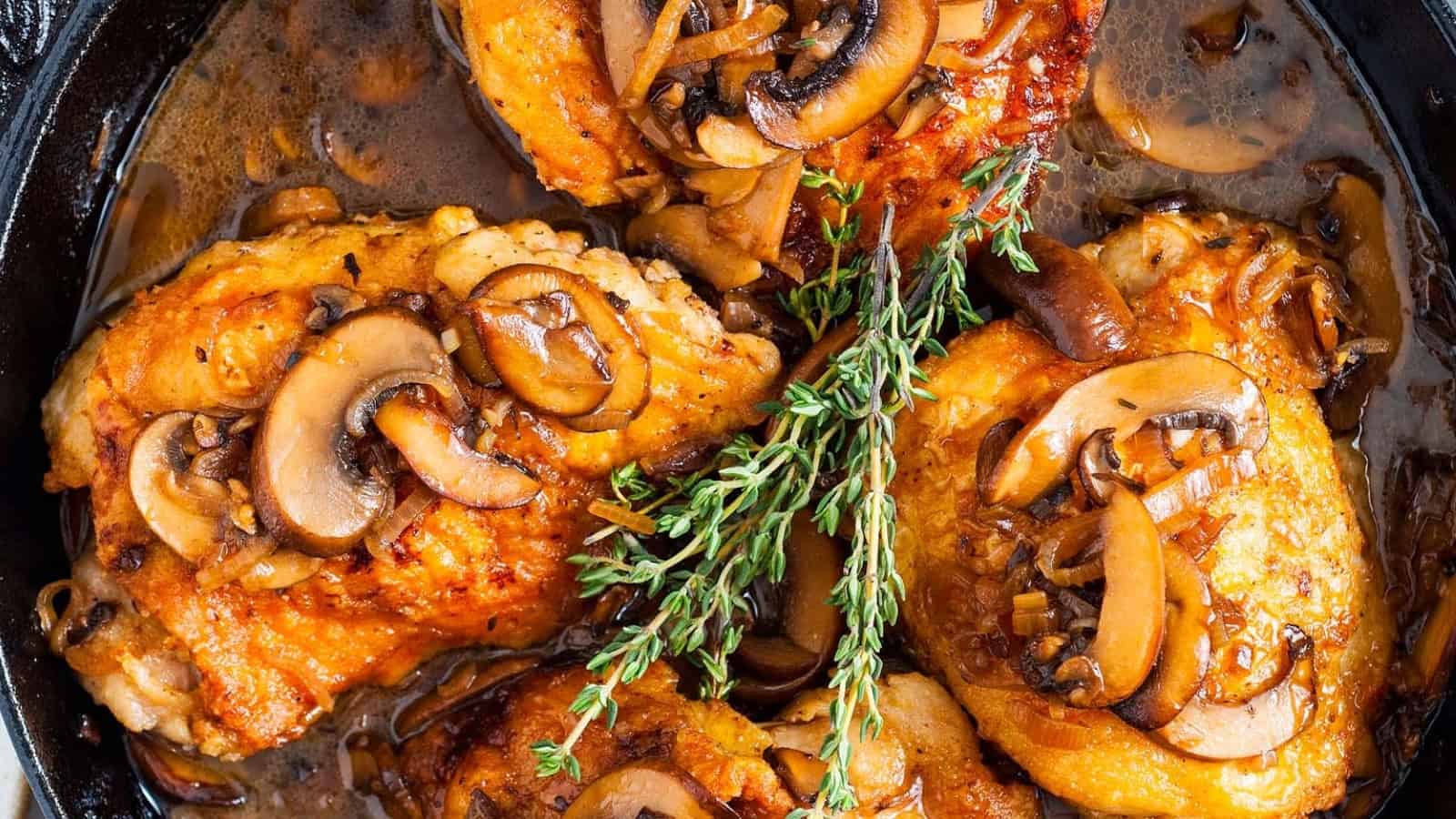 Golden chicken thighs topped with saut&eacute;ed mushrooms and fresh thyme sprigs in a skillet with savory sauce.
