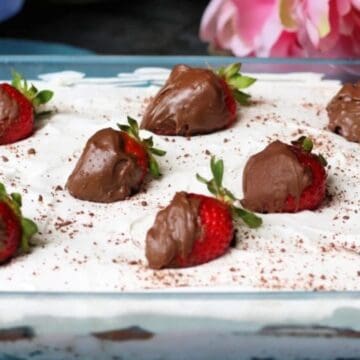 A dessert topped with whipped cream and chocolate-covered strawberries in a glass dish.