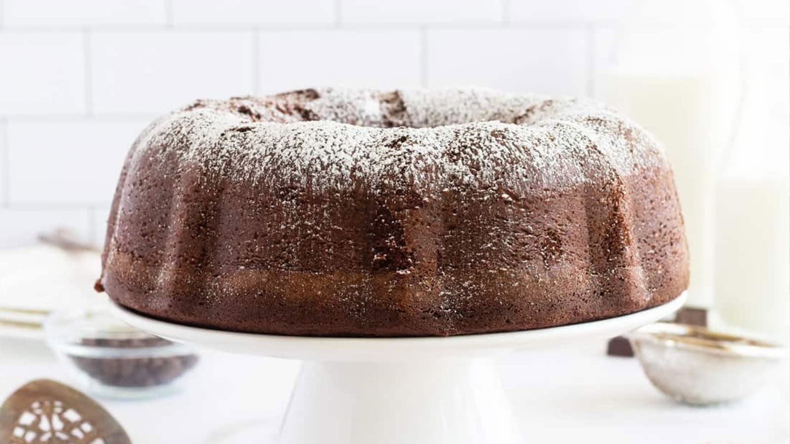 Chocolate bundt cake, a classic among vintage desserts, dusted with powdered sugar on a white cake stand against a light background.