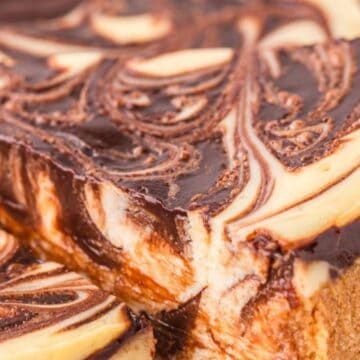 Close-up of a cheesecake slice with a chocolate and vanilla swirl topping and a graham cracker crust.
