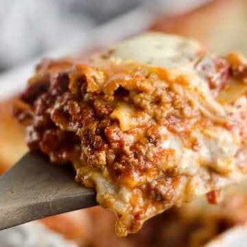 A close-up of a cheesy slice of lasagna being lifted from a baking dish with a spatula.
