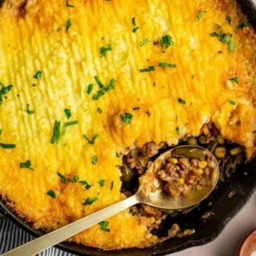 Shepherd’s pie in a cast iron skillet with a serving spoon, garnished with chopped parsley.
