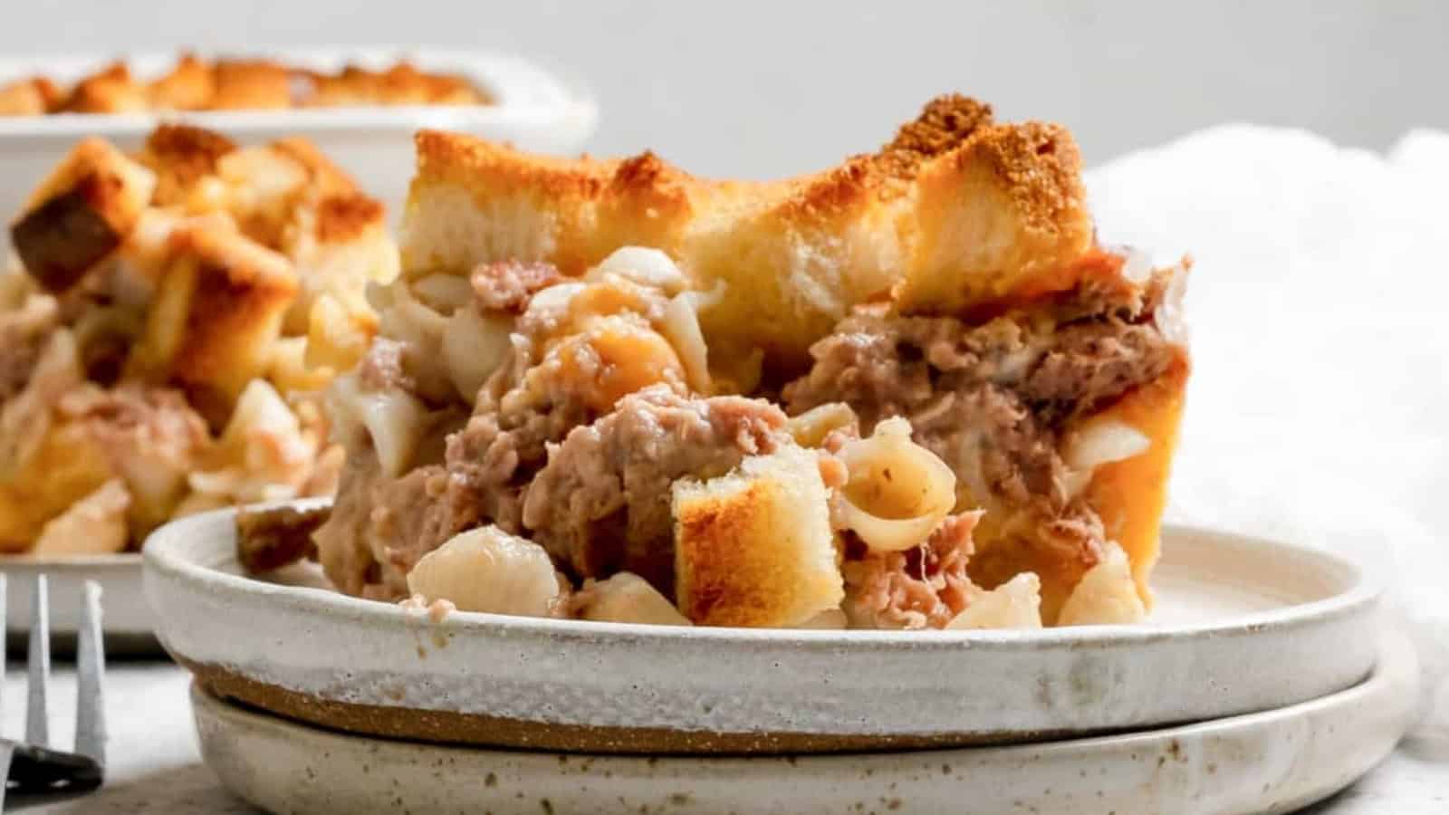 A close-up of tuna casserole with pasta and toasted bread cubes served on a white plate.