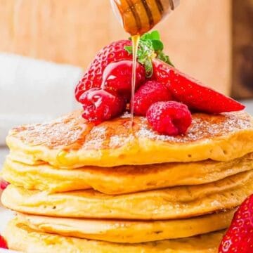 A stack of pancakes topped with strawberries and raspberries, with honey being drizzled on top—one of the perfect Mother's Day brunch dishes.