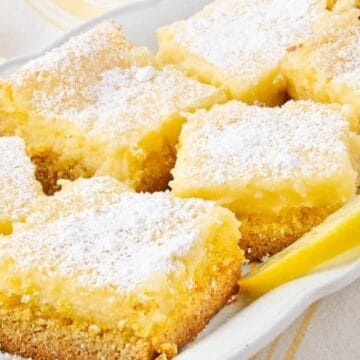 A plate of lemon bars topped with powdered sugar, garnished with lemon slices.