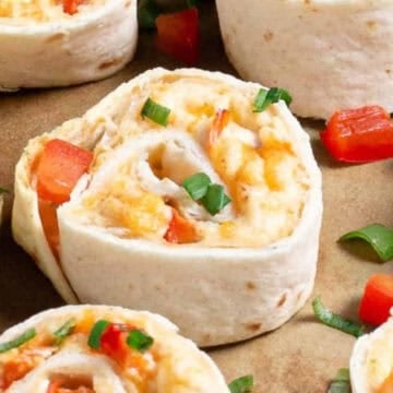 Close-up of tortilla pinwheels with chopped red peppers and green onions, next to a lemon wedge.
