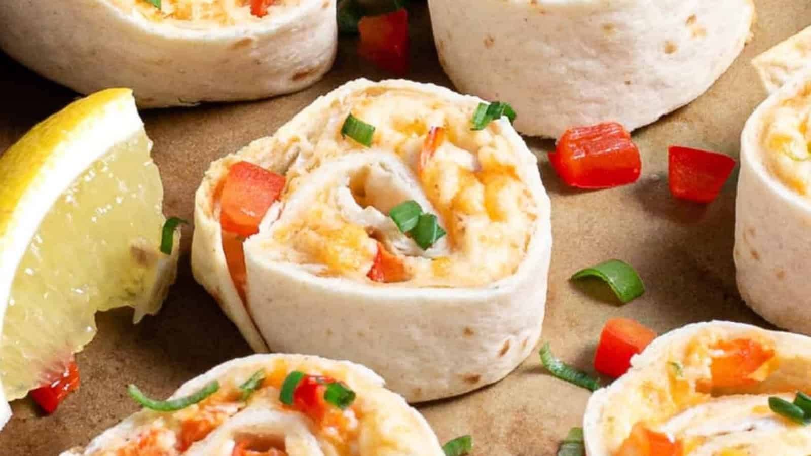 Six tortilla pinwheels with cheese and peppers, garnished with green onions and lemon wedges on a tray.